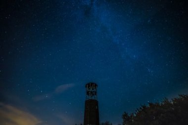 Bir Gözcü Kulesi yıldız ve küçük bulutlar dolu gece gökyüzü altında.