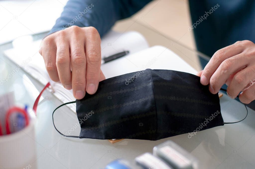 A man use mask at work place for Social distancing. Black mask in hand for protect virus and dust.