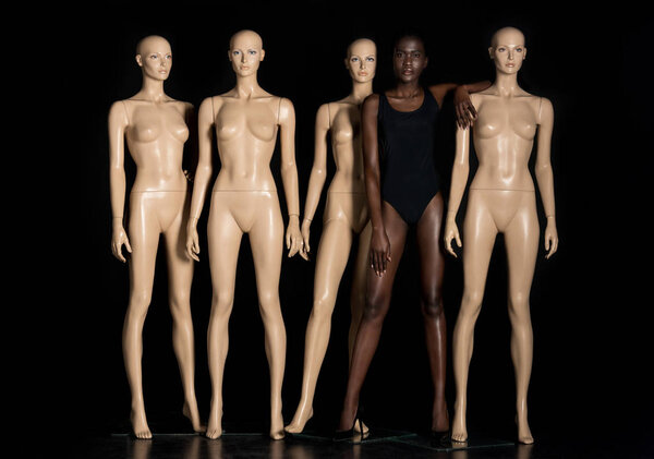 full length view of beautiful young african american woman in swimsuit standing between mannequins and looking at camera on black 
