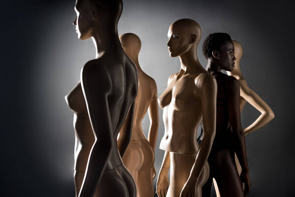 african american woman in swimsuit standing between dummies and looking away on black