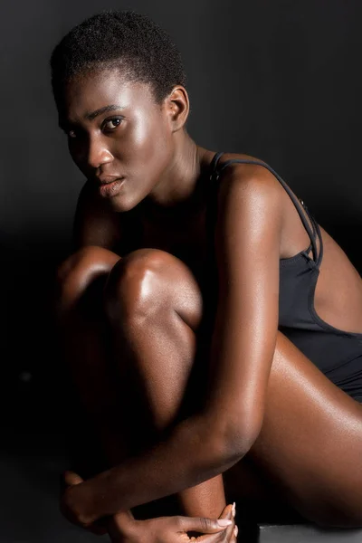 座っていると黒のカメラ目線の水着で魅力的なアフリカ系アメリカ人の女の子  — 無料ストックフォト