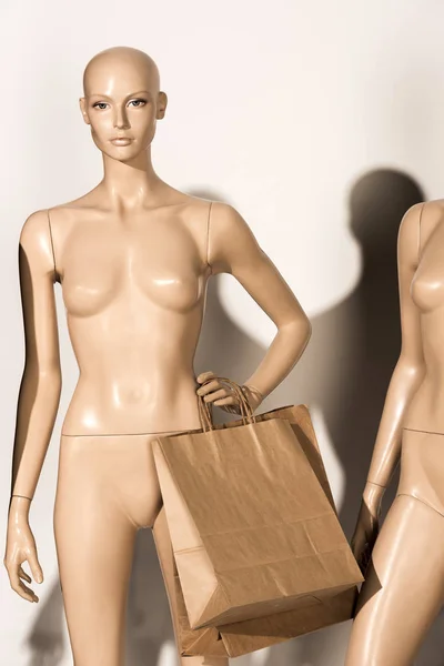 naked bald mannequin with paper bags on white