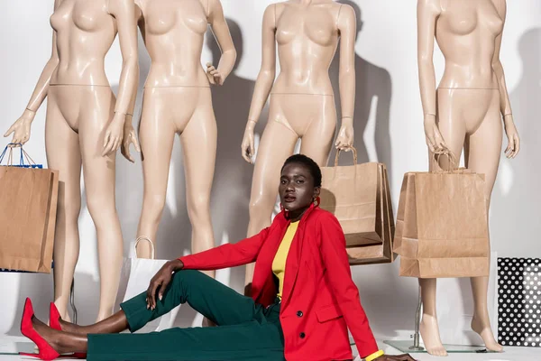 Стильная Африканская Американка Смотрит Камеру Сидя Перед Манекенами Бумажными Пакетами — Бесплатное стоковое фото