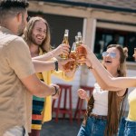Jóvenes felices tintinear botellas de cerveza en el bar de la playa