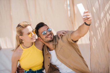 Genç bir çift güneş gözlüğü ile smartphone selfie bungalow alarak gülümseyen 