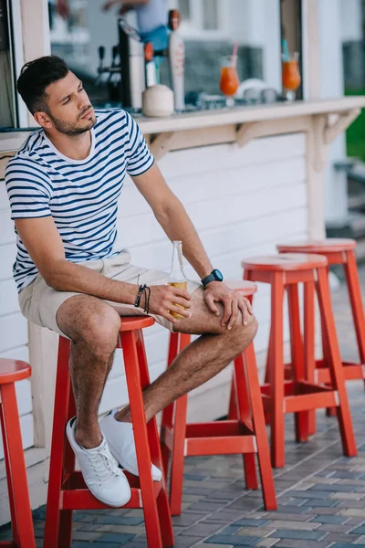 Bonito Jovem Segurando Copo Cerveja Enquanto Sentado Bar Praia — Fotografia de Stock