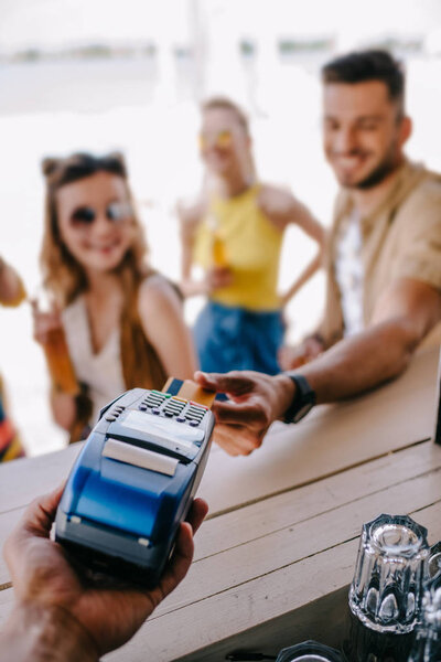 selective focus of young man paying with credit card and payment terminal at beach bar