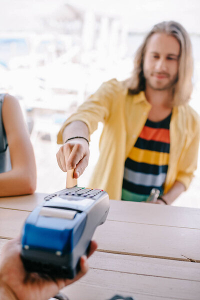 selective focus of young man paying with credit card on terminal at beach bar  