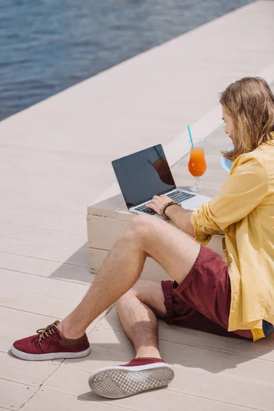 在海滩上使用带空白屏幕的笔记本电脑的年轻人的高角度视图 — 免费的图库照片