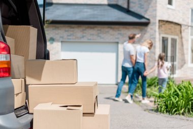 closeup view of cardboard boxes and family holding hands and walking behind in yard of new house  clipart