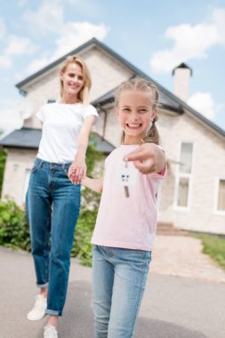 mutlu çocuk gösteren anahtar biblo ile gülümseyen ve yeni evin önünde annenin elini tutarak 