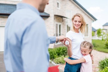 partial view of real estate agent giving key to young woman with daughter in front of new house