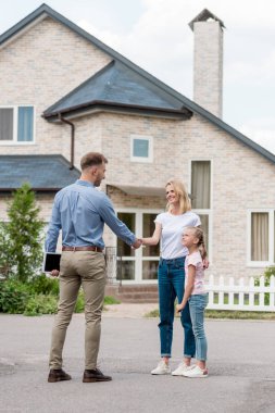 realtor with digital tablet shaking hand of woman with daughter in front of new cottage  clipart