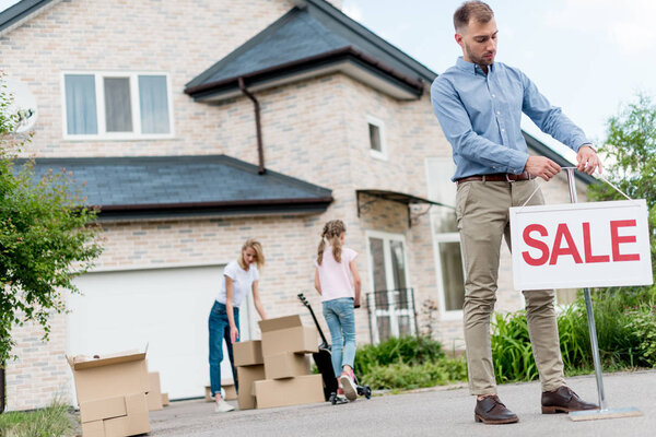 male realtor hanging sale sign in front of people relocating from house