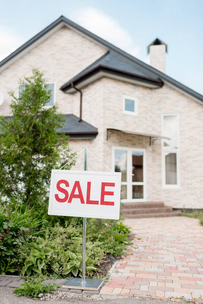wooden placard with sale sign in front of modern cottage