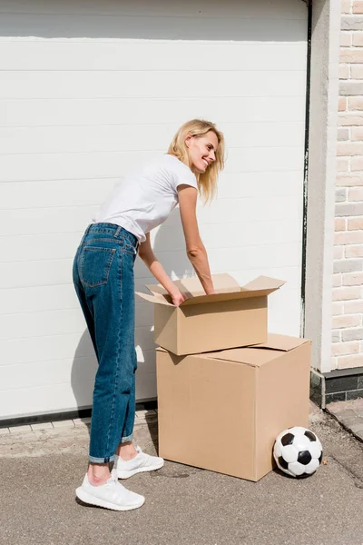 Jovem Mulher Desempacotando Caixas Papelão Perto Bola Futebol Frente Garagem — Fotografia de Stock