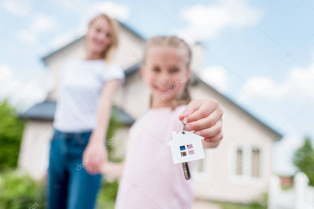 close up view of key with trinket in hand of child holding hand of mother in front of new cottage 