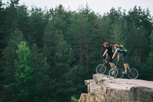 Side View Young Trial Bikers Standing Rocky Cliff Blurred Pine — Stock Photo, Image