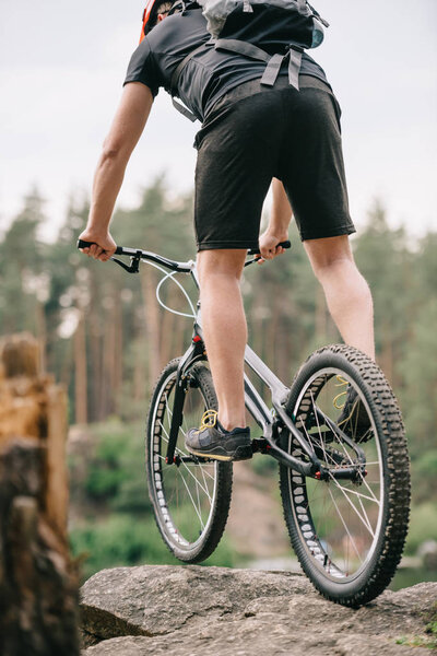 rear view of trial biker balancing on cliff outdoors