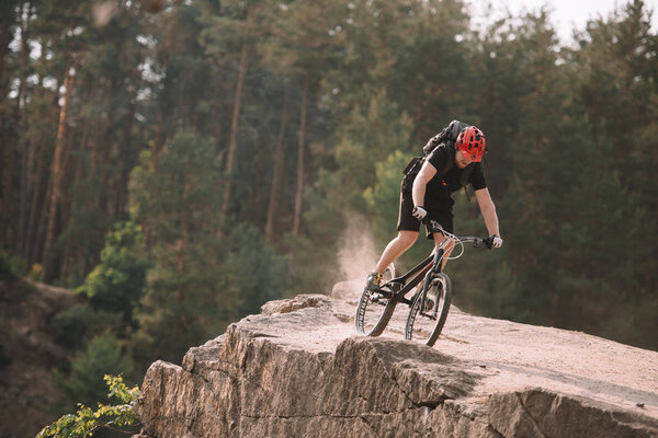 young trial biker riding on rocky clifff outdoors