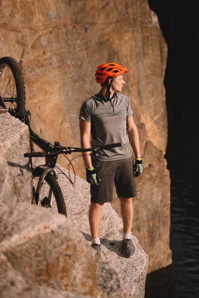 Giovane Biker Prova Piedi Rocce Guardando Lontano All Aperto — Foto stock gratuita