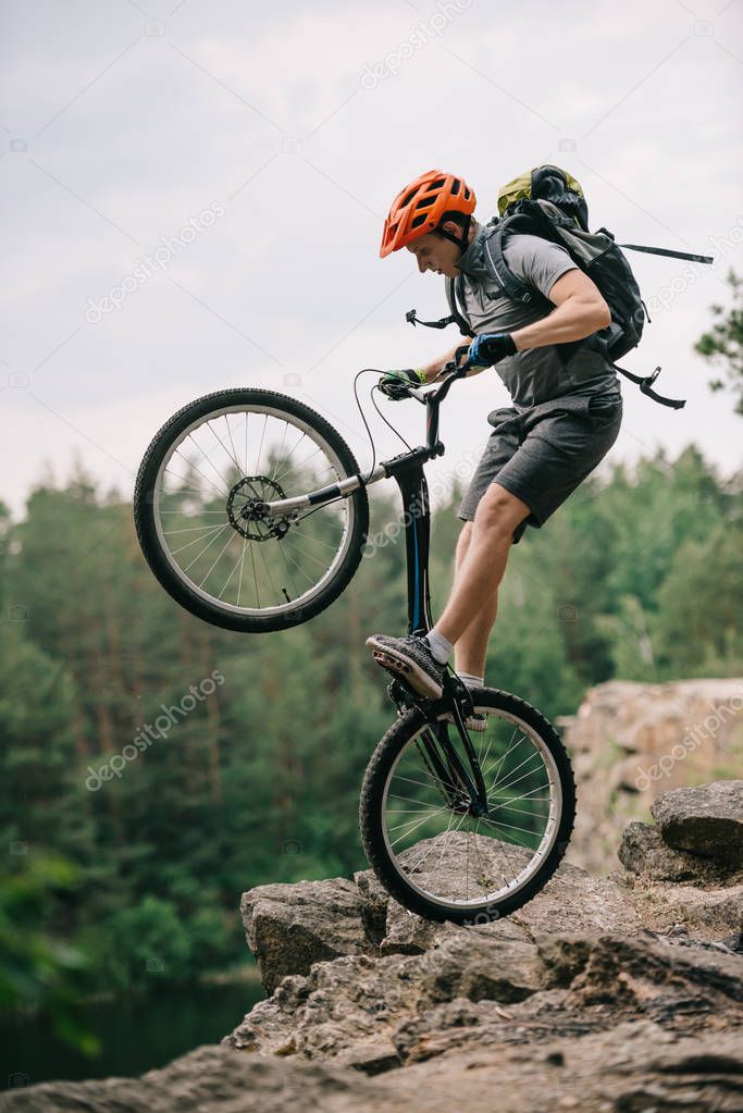 extreme trial biker standing on back wheel on rocky cliff