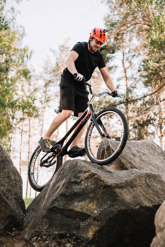 bottom view of young trial biker balancing on rock outdoors