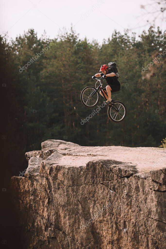 trial biker jumping on bicycle over rocky cliff outdoors