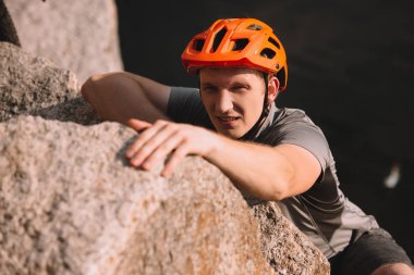 handsome young traveller in helmet climbing on rock and looking at camera clipart