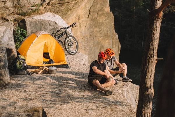 active young bike travellers with canned food sitting on cliff