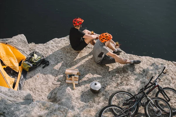 食べてアクティブな自転車旅行者のハイアングル湖の上の岩の崖の上に食べ物の缶詰 — ストック写真