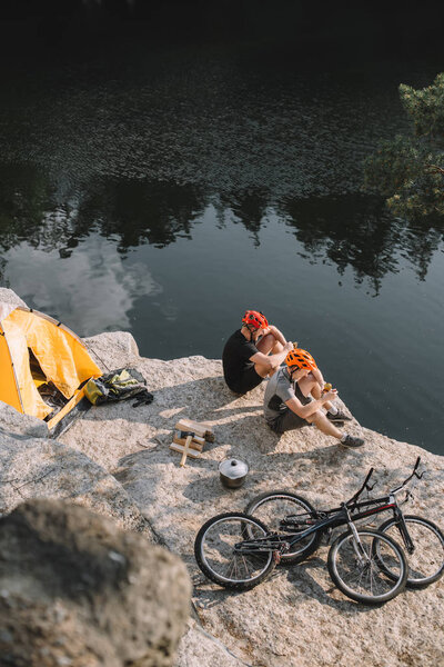 high angle view of young bike travellers eating canned food in camping on rocky cliff