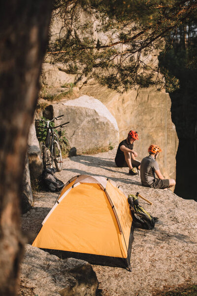 high angle view of trial bikers relaxing on rocky cliff with camping tent