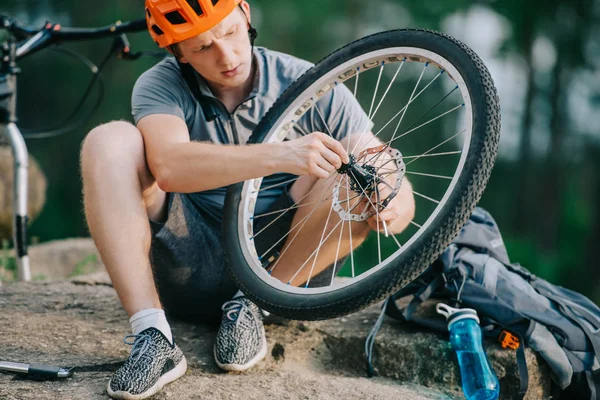 Poważne Młody Rowerzysta Próbnego Mocowania Koła Roweru Zewnątrz Siedząc Kamieniu — Zdjęcie stockowe