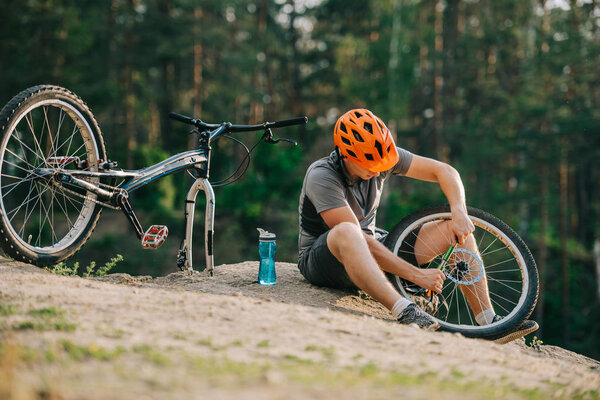 attractive young trial biker pumping wheel of bicycle outdoors