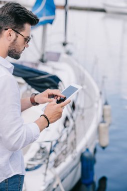 Yat dijital tablet kullanarak güneş gözlüklü genç adam resmini kırpılmış