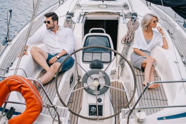 serious young couple in sunglasses looking away while sitting on yacht