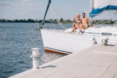 selective focus of wooden pier and young couple on yacht behind clipart