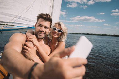 smiling young couple taking selfie on smartphone on yacht  clipart