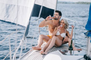 smiling couple in swimwear drinking champagne on yacht  clipart