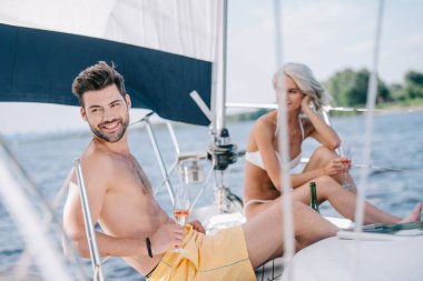 smiling couple in swimwear relaxing with champagne glasses on yacht  clipart