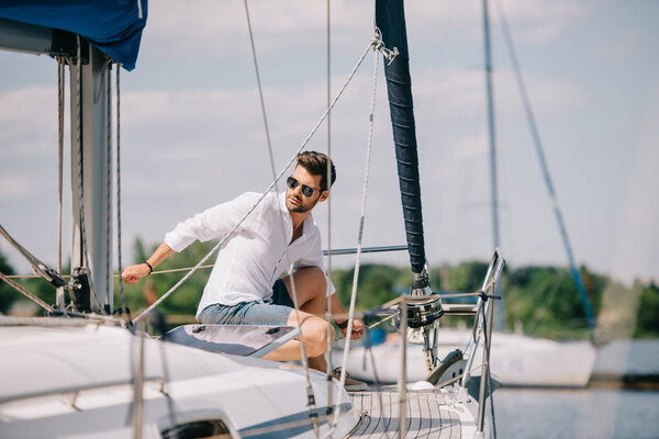 Красивый молодой человек в солнечных очках смотрит в сторону, сидя на яхте
