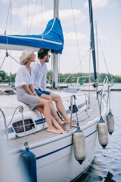 beautiful young couple sitting together on yacht and looking away