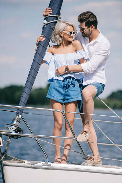 счастливая молодая пара в солнечных очках, обнимающая яхту

