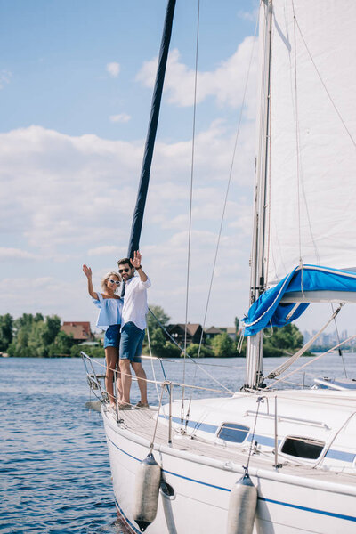 beautiful young couple waving hands while standing together on yacht