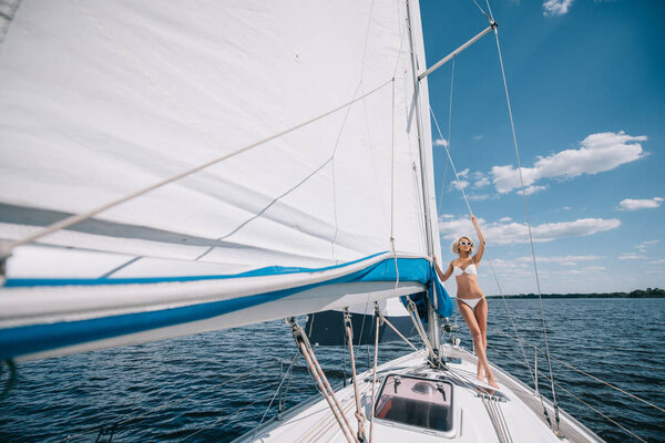 distant view of attractive young woman in swimwear standing on yacht 