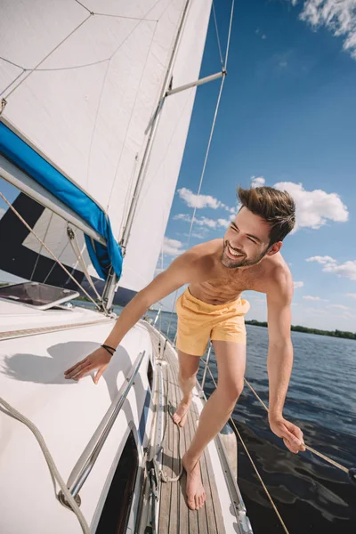 ヨットの上で実行しているトランクの水着で上半身裸の男の笑みを浮かべてください — ストック写真