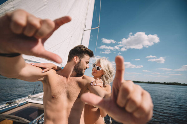 selective focus of shirtless man gesturing by hands and talking to smiling girlfriend on yacht 