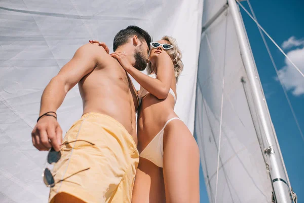 ヨットの上でビキニの魅力的なガール フレンドを抱きしめる笑顔の上半身裸の男の低角度のビュー — ストック写真
