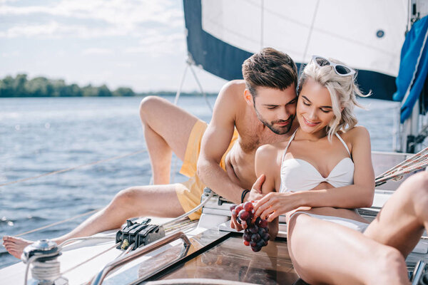 happy young couple in swimwear relaxing and eating grapes on yacht 